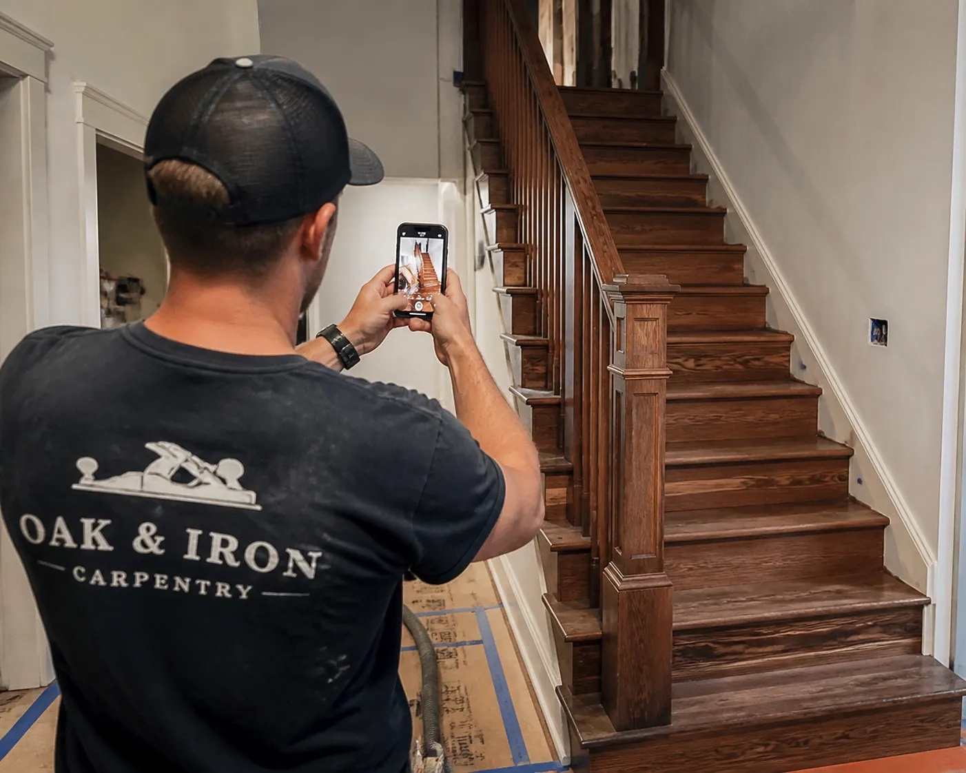 Carpenter photographing a finished custom staircase to update his Google Business Profile with real work.